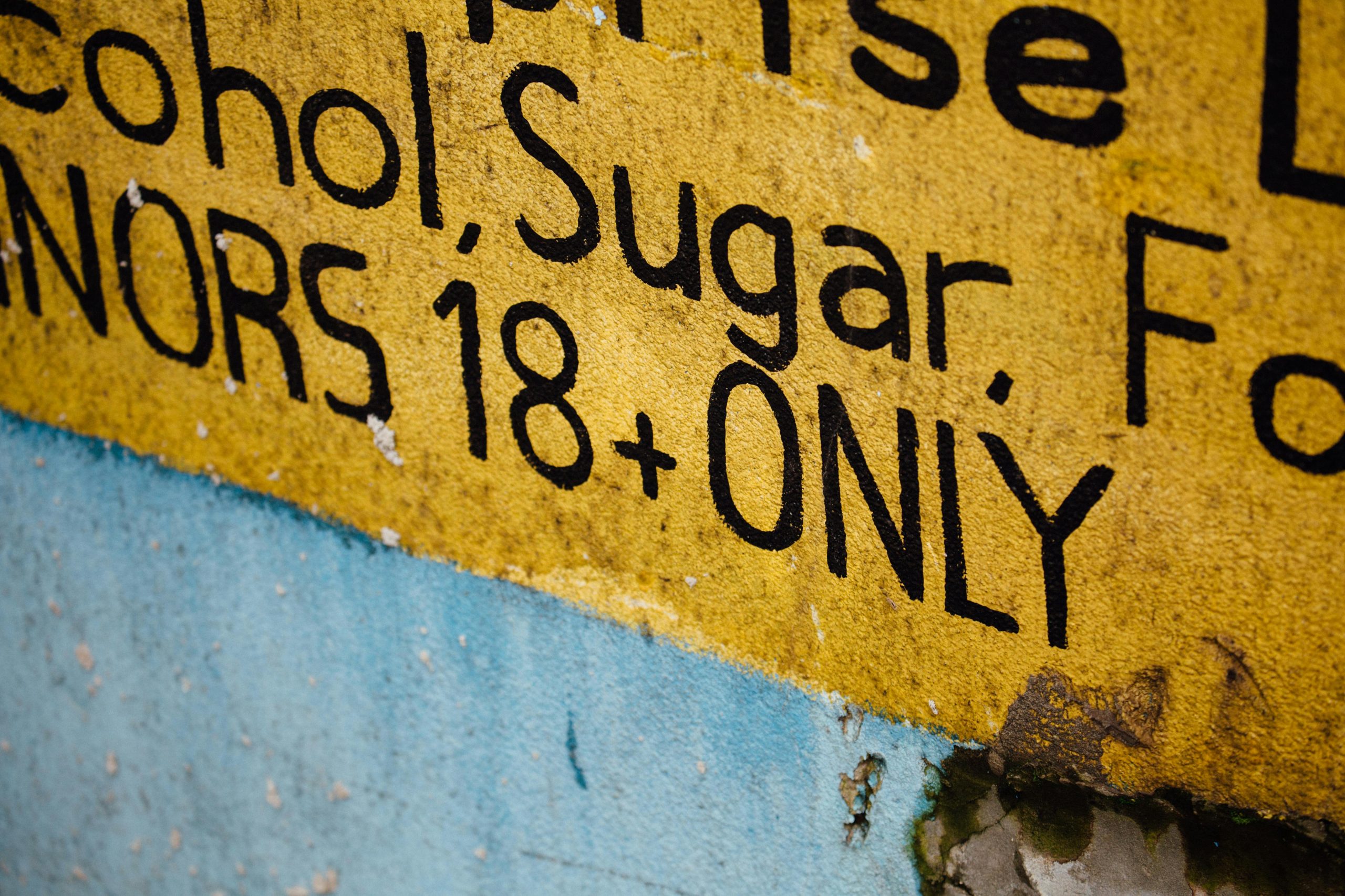 Yellow warning sign stating 'MINORS 18+ ONLY' with visible text and textured background.