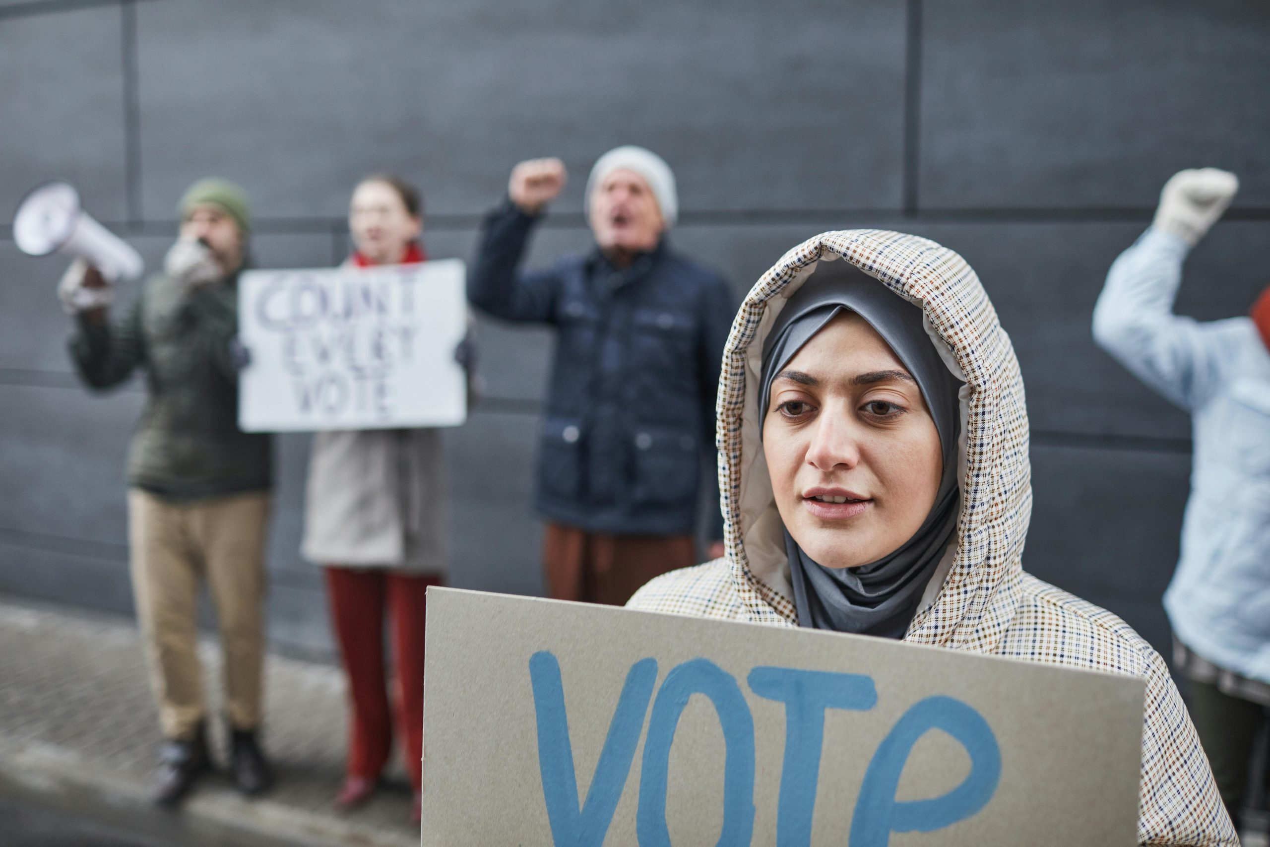 Close-up of a woman in a hijab holding a 'Vote' sign at a peaceful street protest advocating democracy.